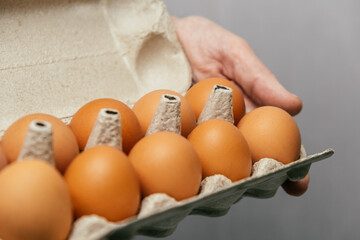 person is holding carton fresh brown eggs in kitchen. eggs are nestled in their compartments, ready for cooking or baking activities. close up.