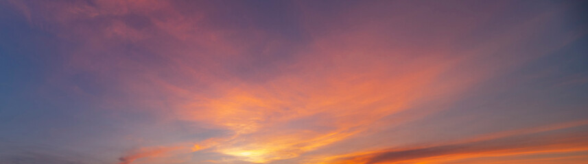 A beautiful sunset sky with dramatic and colorful clouds during twilight. The vibrant gradient of orange, purple, and blue creates a peaceful and romantic atmosphere, perfect for nature backgrounds an