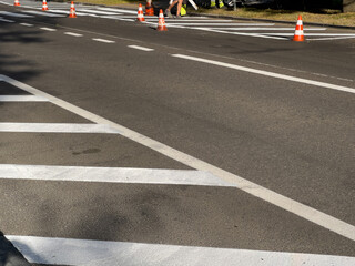 Workers manage road maintenance with traffic cones marking lane changes on a busy urban street in bright daylight