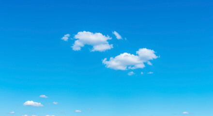 Fluffy white clouds drift across a brilliant blue sky on a clear sunny day