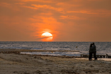 Fototapeta premium Saint-Aubin-Sur-Mer, France - 08 07 2025: View the silhouette of a happy couple on the beach just in front of the sunset and golden hour