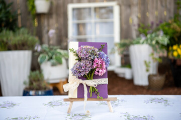 Elegant purple book tied with lace and fresh hydrangeas on a table in a sunny backyard, perfect for garden parties, book clubs, and romantic outdoor gatherings.