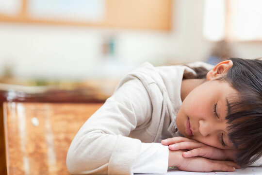 Asian girl student sleeping with folded arms on wooden desk and notebook in classroom copy space - Powered by Adobe