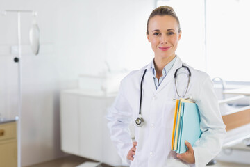Mid adult doctor standing in hospital holding files, wearing lab coat and stethoscope, copy space
