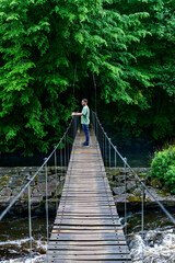 Fototapeta premium Mann steht auf Hängebrücke über Fluss Mörrumsån mitten im Wald in Blekinge Schweden