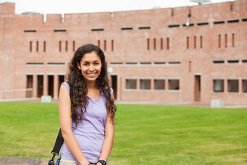 Female student smiling while standing on campus quad checking wristwatch with backpack, copy space