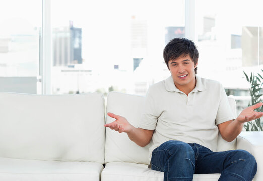 Man shrugging on white sofa in living room with potted plant and city skyline, copy space