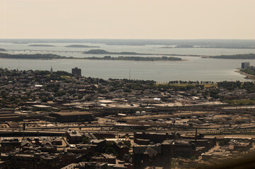 Fototapeta premium Dive into this vibrant aerial view of a coastal urban landscape. The city boasts a grid-like layout of residential and industrial buildings, split by a river or bay. A prominent bridge stretches