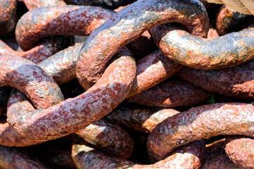 Close-up shot of weathered, rusted metal chains with varied colors from reddish-brown to orange and gray. Thick, robust links showcase heavy-duty wear and texture, with pits and flakes from erosion