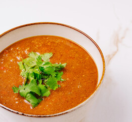 Delicious bowl of soup garnished with fresh cilantro on a white background