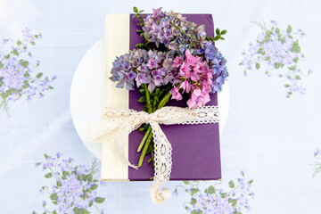 Obraz premium Charming floral book centerpiece with hydrangeas and lace ribbon, set against a lush backyard backdrop for garden-themed events and literary gatherings.