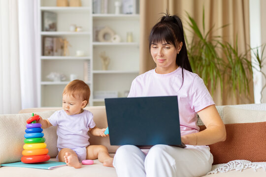 Mother working on laptop while baby girl plays with colorful toys nearby. Lifestyle portrait of modern motherhood, childcare, multitasking and family love at home