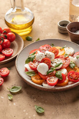 Caprese salad with sliced tomatoes, mozzarella, basil, olive oil on brown textured background