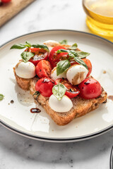 Caprese sandwich or toast with mozzarrella balls, cherry tomatoes, olive oil and basil leaves close up. Healthy vegetarian breakfast, snack or lunch. White marble background