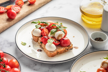 Caprese sandwich or toast with mozzarrella balls, cherry tomatoes, olive oil, pepper and fresh basil leaves. Healthy vegetarian breakfast, snack or lunch. White marble background