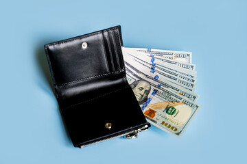 black wallet with dollars hundred dollar bills sticking out of black wallet on blue background with space for text