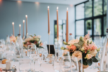Elegant wedding dinner table with lit candles, floral arrangements, wine glasses and romantic ambiance for celebration reception in luxury venue.