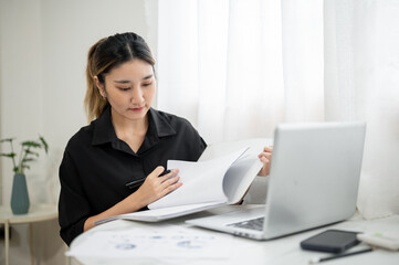 Smart asian businesswoman office worker holding pen reading document in file folder at working table