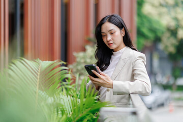 Businesswoman using smartphone near office building with plants