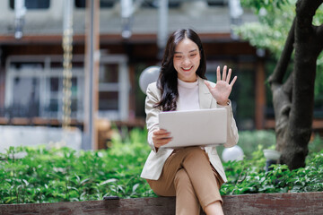 Asian businesswoman video calling and waving outdoors