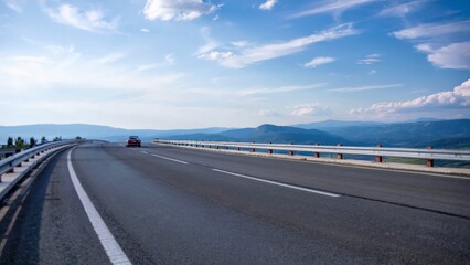 A Single Car Traveling on a Scenic Mountain Highway Under a Beautiful Blue Sky: Representing a Summer Road Trip, Vacation Journey, or the Freedom of the Open Road