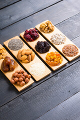 sun dried organic fruits, nuts and oil seeds on bamboo serving tray, black wooden table background