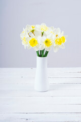 white daffodils at china vase on bright wood table