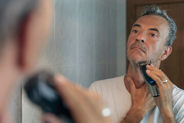 
Mature man shaving in front of a mirror with an electric razor