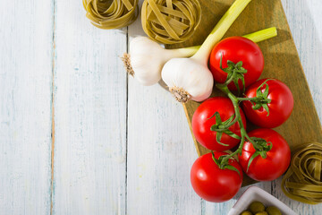 fresh tomato, garlic, olive, uncooked tagliatelle pasta on white wooden table, top view