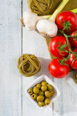 fresh tomato, garlic, olive, uncooked tagliatelle pasta on white wooden table, top view