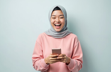 Happy asian muslim woman in hijab, pink shirt using mobile phone. Received good news, laughing. Cheerful student holds smartphone, gets positive emotions isolated on white background. Online