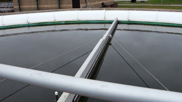 Clarifier pond at a wastewater treatment plant processes water as solids settle and liquid flows, capturing the industrial treatment process in motion.