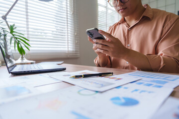 Businessman using smartphone and analyzing financial charts at office desk