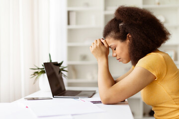 Stressed African American woman sitting with closed eyes at desk with laptop. Concept of emotional burnout, online work fatigue or difficult study challenges