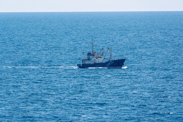 Fishing boat in blue sea and clear sky with birds flying overhead.