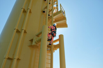 Offshore Rigger Technician Climbing Yellow Wind Turbine Monopile Ladder During Wind Farm Construction Maintenance, GWO Work On Height