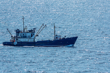 Fishing boat in blue sea and clear sky with birds flying overhead.