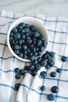 Fresh blueberries spilling from a white bowl on a cloth