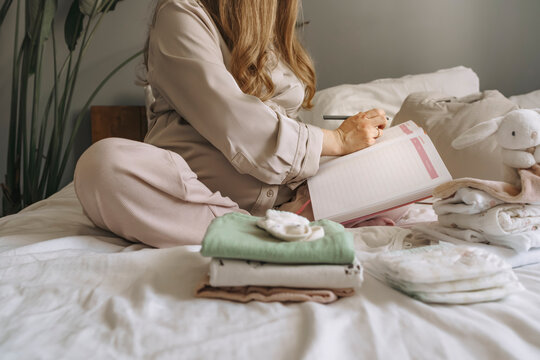 Pregnant person preparing hospital bag and checklist at home in bed