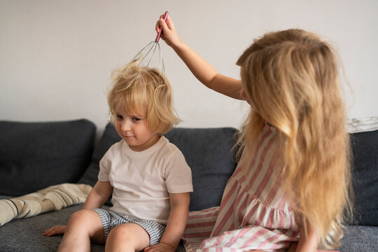 Siblings playing with head massager on sofa indoors in living room