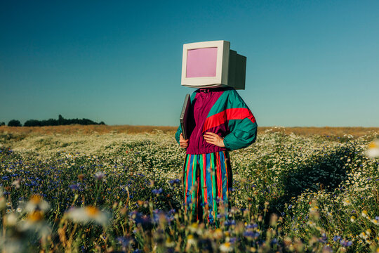 Person with CRT monitor head in 90s track suit on summer meadow