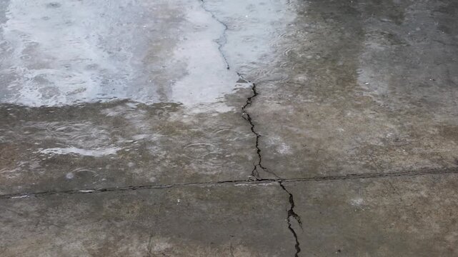 close up of raining water drop on the cement ground with cracks with light and shadow, creating ripples on the ground, sllightly flooding