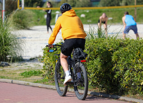 A man in a yellow hoodie is riding a bicycle down a street