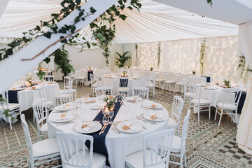 Bright wedding marquee with round tables, draped ceiling and fairy light garlands