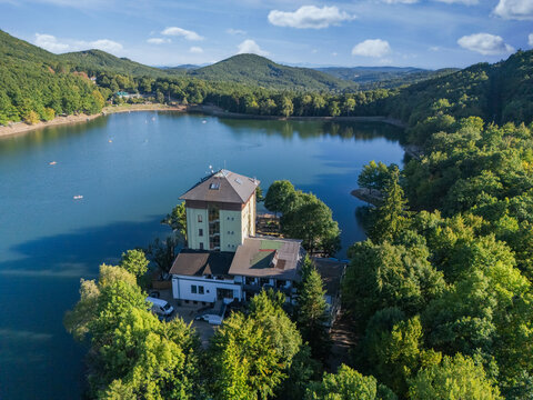 Aerial view of a building complex on a peninsula surrounded by tranquil waters and verdant forests, reflecting the clear sky, Pocuvadlo lake, Banskobystrick&Atilde;&frac12; kraj, Slovakia.