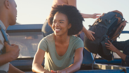 Group Of Friends Unloading Backpack From Pick Up Truck On Road Trip To Cabin In Countryside