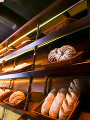Wide variety of fresh baked breads on display: sourdough, baguettes, braided loaves, and rustic rounds, neatly arranged in wicker baskets at a warm, wood-accented local bakery cafe in Hoi An