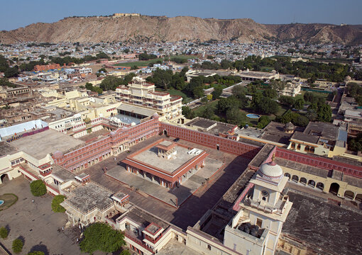 Aerial view of the rosy-hued City Palace complex basking in the sun's glow, contrasted against the arid hills in the distance, Jaipur, Rajasthan, India.