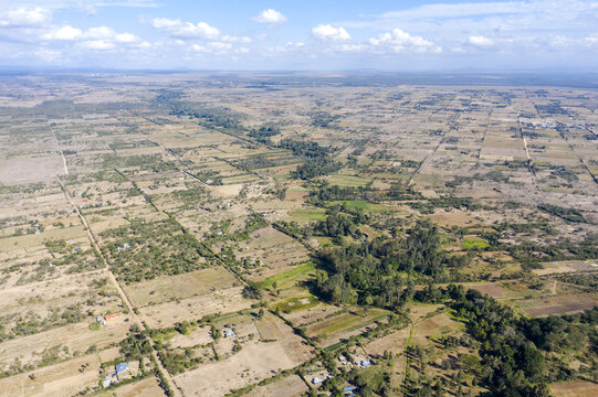 Aerial view of a tapestry of earth unfolds in geometric patterns, stitched together by green vegetation and scattered homes, Nanyuki, Kenya.