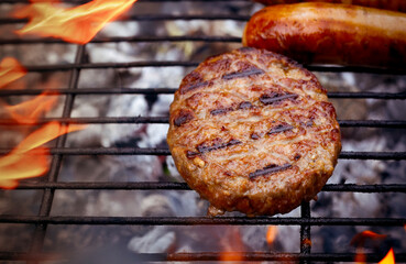 Close-up of a flame-grilled juicy hamburger , sausage on a BBQ grill, sizzling with summer vibes. A mouthwatering, indulgent scene perfect for outdoor meals and food photography.